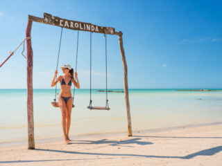 Girl with blue bikini sitting on a wooden swing in front of the Caribbean Sea on Holbox Island